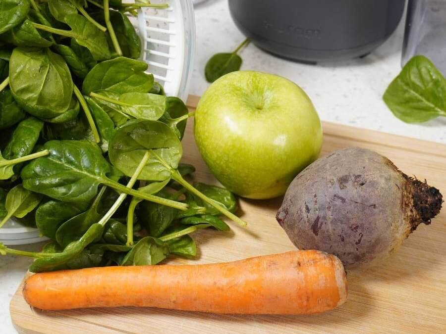 Spinach, carrot, apple and beetroot placed on kitchen table in front of Hurom H310A slow juicer, ready to be juiced