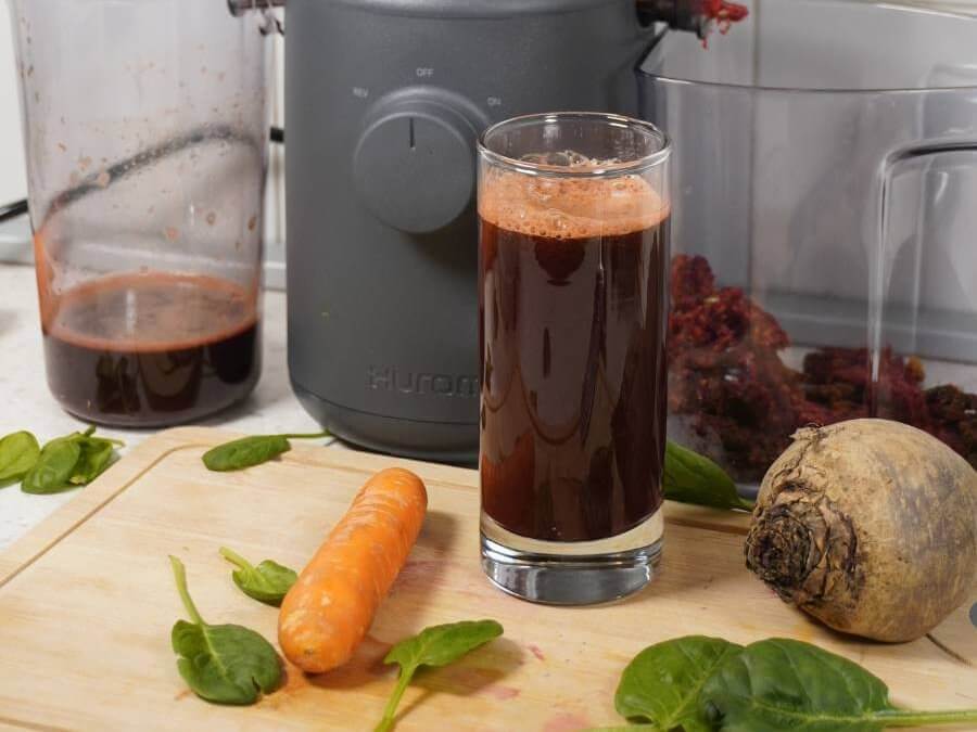 apple, carrot, spinach & beetroot juice in a glass in front of hurom slow juicer H310